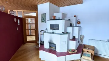 Wohnbereich mit traditionellem Kachelofen, Holzboden und Holzdecke, der eine warme Atmosphäre schafft.