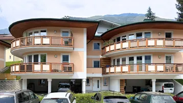 Mehrfamilienhaus mit mehreren Balkonen und Blick auf die umliegende Berglandschaft.