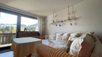 Gemütliches Wohnzimmer mit Rattanmöbeln, Bergblick und Zugang zum Balkon.