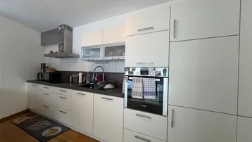 Moderne Einbauküche mit weißen Schränken, dunkler Arbeitsplatte und integrierten Geräten.