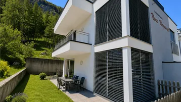 Moderne Wohnanlage mit gepflegtem Rasen, Terrasse und Bergblick im Hintergrund.
