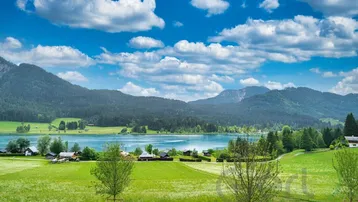 Malerischer Panoramablick auf einen blauen See umgeben von grünen Wäldern und Bergen.