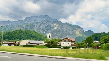 Weitläufige Landschaft mit majestätischen Bergen im Hintergrund und grünen Wiesen im Vordergrund.