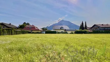Weitläufige Grünfläche mit Blick auf die umliegende Berglandschaft und benachbarte Häuser.