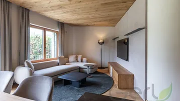 Gemütliches Wohnzimmer mit beigem Sofa, Holzboden und Blick ins Grüne durch große Fenster.
