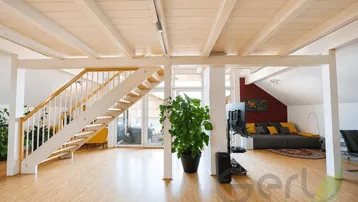 Heller, offener Wohnbereich mit sichtbaren Holzdeckenbalken und einer eleganten Holztreppe.