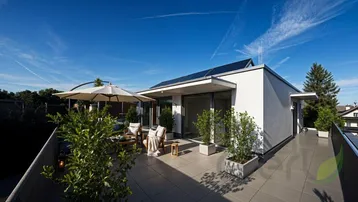 Moderne Architektur mit großer Dachterrasse, Photovoltaikanlage und weitem Blick in die grüne Umgebung.