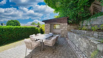 Sonniger Terrassenbereich mit Esstisch, Stühlen und Steinmauer im Garten.