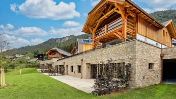 Moderne Chalet-Architektur mit Steinfassade, Holzverkleidung und Bergblick in grüner Umgebung.