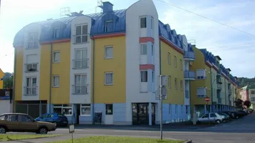 Mehrstöckiges Gebäude mit gelber Fassade, blauen Akzenten und Mansarddach in städtischer Umgebung.
