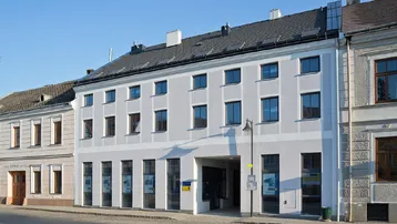 Mehrstöckiges Gebäude mit hellgrauer Fassade und vielen Fenstern an einer städtischen Straße.