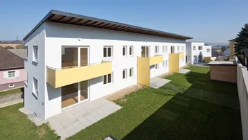 Moderne Wohnanlage mit weißen Fassaden, gelben Balkonen und grünen Rasenflächen in ländlicher Umgebung.