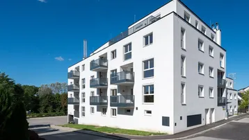 Modernes weißes Mehrfamilienhaus mit klaren Linien und zahlreichen Balkonen unter blauem Himmel.