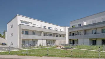 Moderne Wohngebäude mit Balkonen und einem gemeinschaftlichen Grünbereich mit Spielplatz.