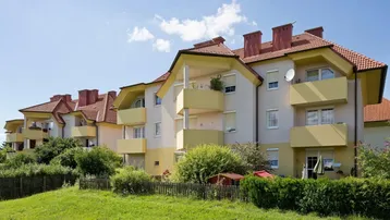 Reihe von Mehrfamilienhäusern mit hellen Fassaden, roten Dächern und grüner Umgebung.