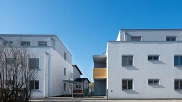 Moderne Wohngebäude mit weißer Fassade unter klarem blauem Himmel.
