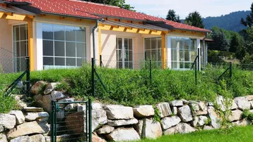 Neubau mit großen Fenstern, rotem Ziegeldach und einem naturnahen Steingarten.