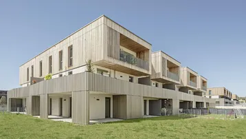 Moderne Wohnanlage mit Holzfassade, Balkonen und großzügigen Grünflächen.