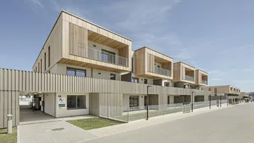 Moderne Reihenhäuser mit Holzfassade und Balkonen unter blauem Himmel.
