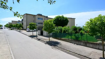Mehrere moderne Wohngebäude entlang einer ruhigen Straße mit Bäumen und Grünflächen.