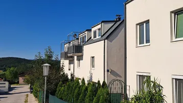 Moderne Mehrfamilienhäuser mit Balkonen und gepflegter Hecke unter blauem Himmel.