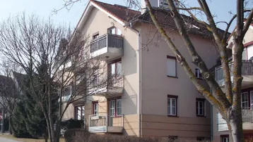 Mehrfamilienhaus mit beiger Fassade, Satteldach und mehreren Balkonen in einer ruhigen Wohngegend.