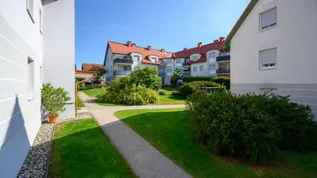 Grünanlage mit Gehwegen zwischen Wohngebäuden, umgeben von gepflegten Büschen und Bäumen.