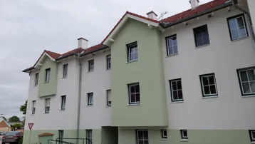 Außenansicht eines modernen Gebäudes mit weißer und grüner Fassade sowie einem Satteldach.