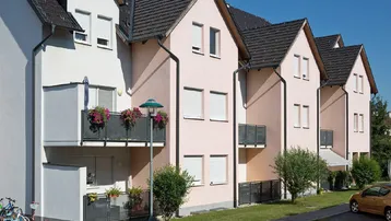 Reihenhäuser mit hellrosa und weißen Fassaden, Balkonen und Satteldächern unter blauem Himmel an einem sonnigen Tag.