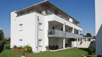Modernes Mehrfamilienhaus mit weißer Fassade, Balkonen und einem kleinen Gartenbereich.