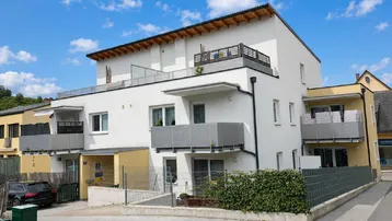 Modernes Mehrfamilienhaus mit weißer und gelber Fassade sowie mehreren Balkonen und Dachterrasse.