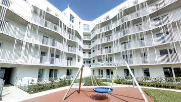 Modernes Wohngebäude mit weißer Fassade und einem Spielplatz im Innenhof.