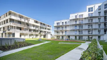 Zwei moderne Wohngebäude mit gepflegter Grünfläche und kleinem Spielbereich im Freien.