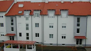 Ansicht einer modernen Wohnanlage mit hellgrauer Fassade und roten Ziegeldächern.