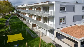 Modernes Mehrfamilienhaus mit Balkonen, Grünflächen und einem kleinen Spielbereich im Freien.