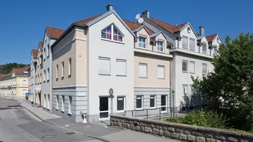 Mehrfamilienhaus mit Satteldach und Rollläden an einer ruhigen Straße gelegen.