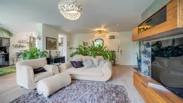 Helles Wohnzimmer mit bequemen Sofas, Holzboden und vielen Pflanzen, die eine gemütliche Atmosphäre schaffen.