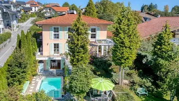 Idyllische Villa mit großem Garten, Pool und Wintergarten, umgeben von viel Grün und Bergblick.