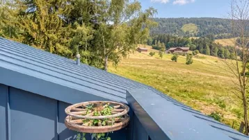Dachbereich des Gebäudes mit Blick auf die umliegende grüne Hügellandschaft und Wälder.