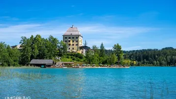 Historisches Gebäude am Ufer eines klaren Sees, umgeben von üppiger Natur und mit privatem Seezugang.