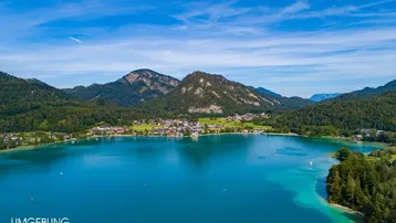 Spektakuläre Luftaufnahme eines malerischen Sees mit einer kleinen Stadt am Ufer, eingebettet in eine Berglandschaft.