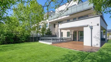 Moderne Hausfassade mit großem Garten, Holzterrasse und überdachtem Außenbereich.
