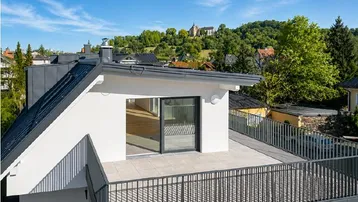 Große Dachterrasse mit Fliesenboden und Blick auf die grüne Umgebung und entfernte Gebäude.