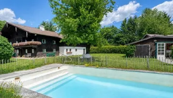 Außenansicht eines traditionellen Hauses mit großem Garten und privatem Swimmingpool unter blauem Himmel.