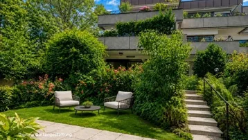 Gepflegter Gartenbereich mit Sitzgelegenheiten und üppiger Bepflanzung vor dem Gebäude.
