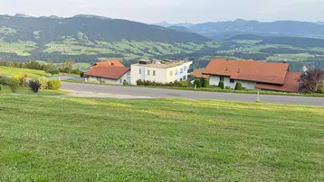 Panoramablick auf eine ländliche Wohnsiedlung mit modernen und traditionellen Häusern vor einer Bergkulisse.