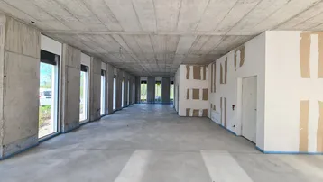 Großer, offener Raum im Rohbau mit Betonwänden und -decken, vielen Fenstern und vorbereiteten Trockenbauwänden.
