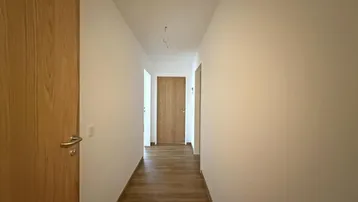 Langer, heller Flur mit Holztüren und modernem Laminatboden, der zu weiteren Räumen führt.
