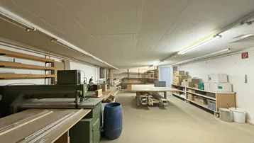 Geräumiger Werkstattbereich mit Holzbearbeitungsmaschinen und Lagerregalen, gut beleuchtet und funktional.