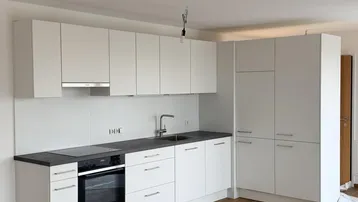 Moderne Einbauküche in Weiß mit dunkler Arbeitsplatte und Laminatboden in einem offenen Wohnbereich.